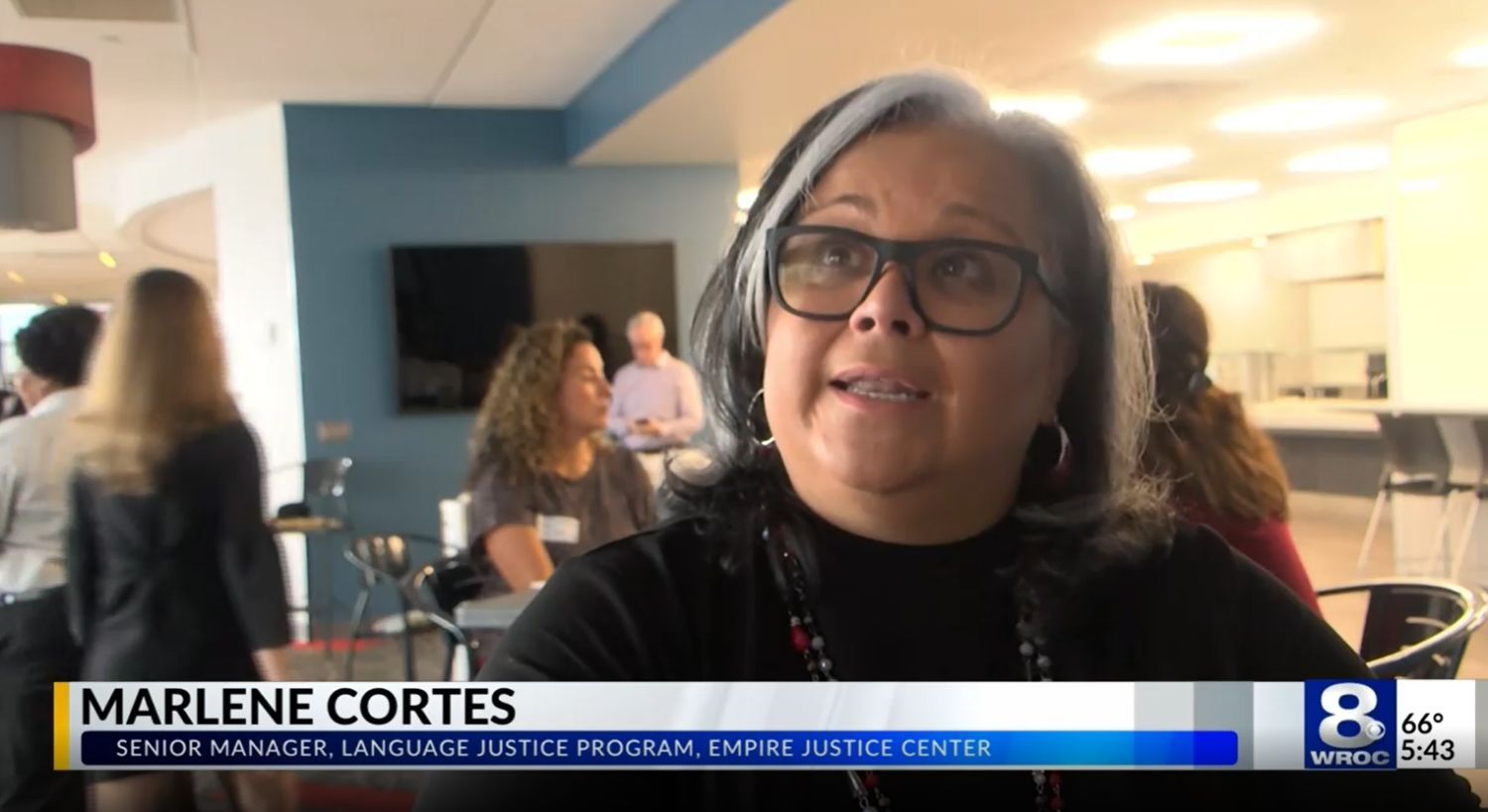 Marlene Cortes being interviewed by WROC Rochester. She is a Latina woman with a cool grey streak in her hair and glasses.