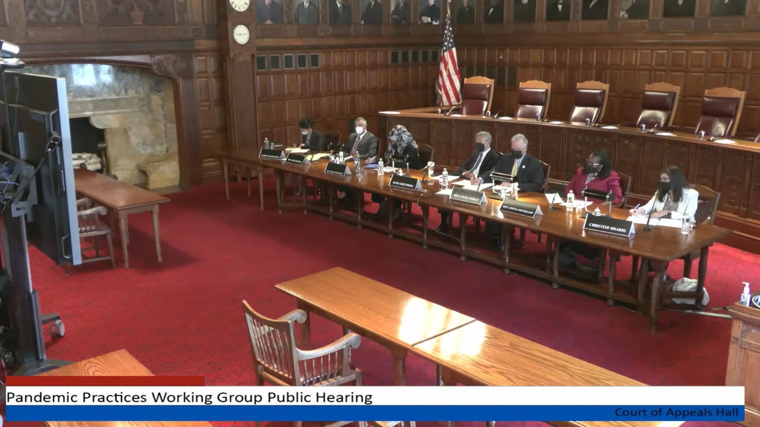 People sitting at long, wooden table to hear testimony on the future of NYS courts. It all looks very fancy.