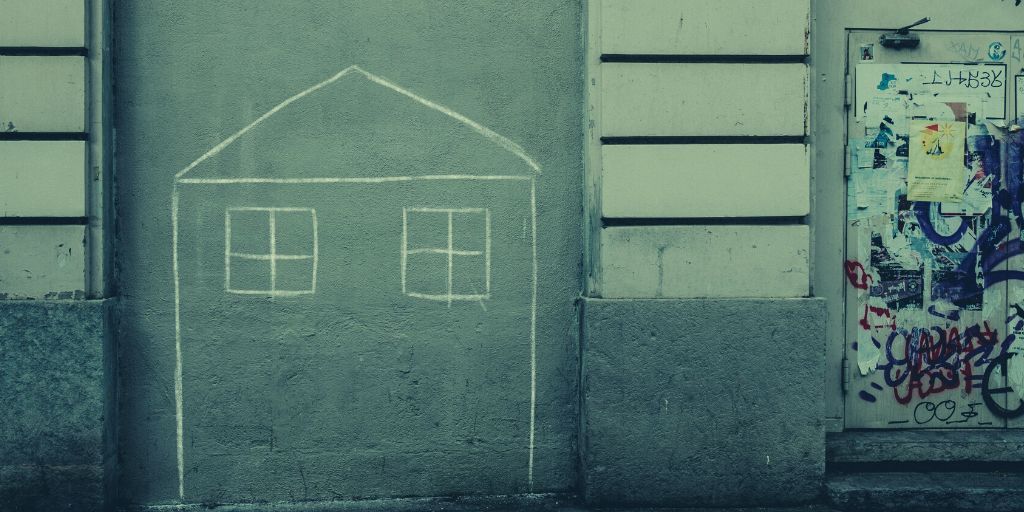 Image of a dilapidated building. On one wall is a child's drawing of a house done in chalk.